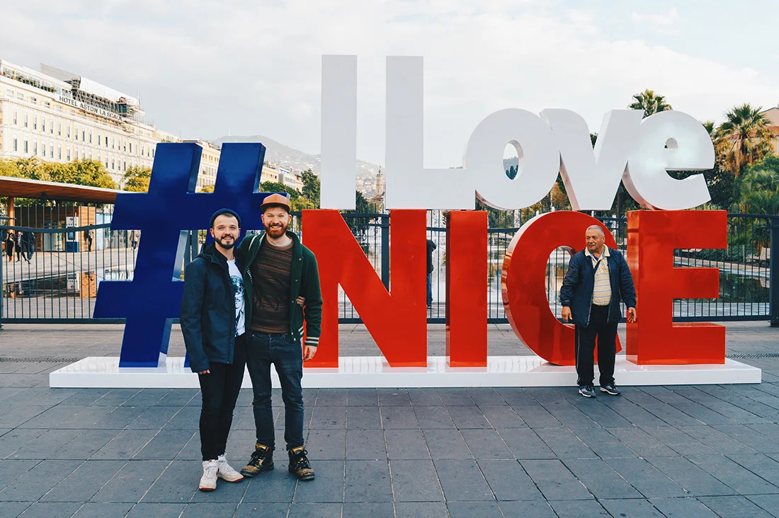 Gay Couple Travel France City Weekend Nice two gay guys in front of the #ILOVENICE sign in the city center of Nice