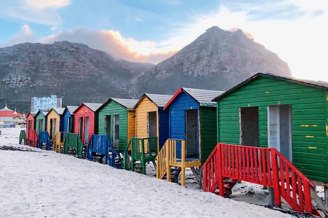 The world-famous colored beach houses of Muizenberg Beach in front of the Muizenberg Mountains © Coupleofmen.com