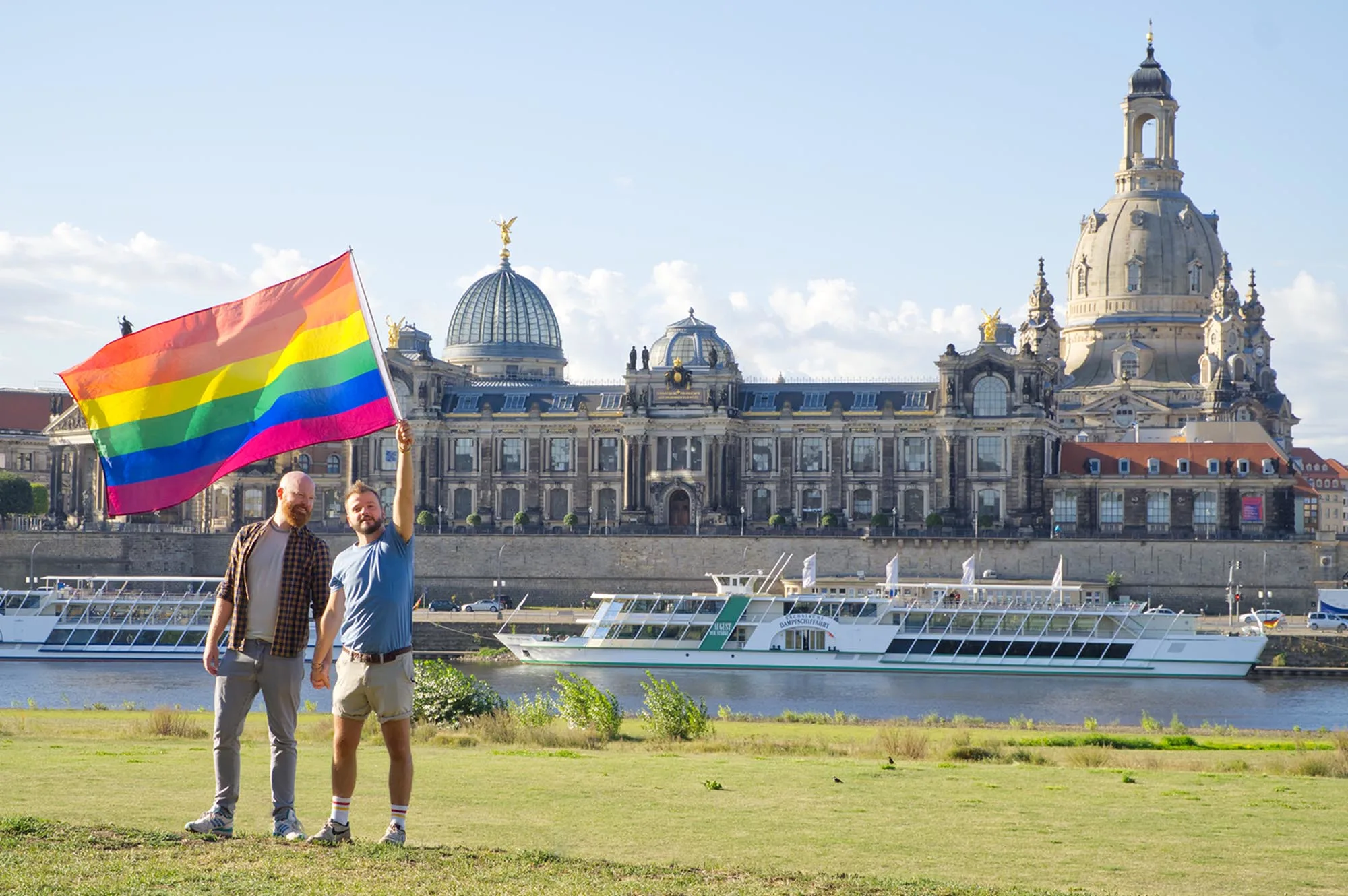 Dresden Gay City Trip Couple of Men with a rainbow flag in front of the Panorama-Dresden Altstadt © Coupleofmen.com