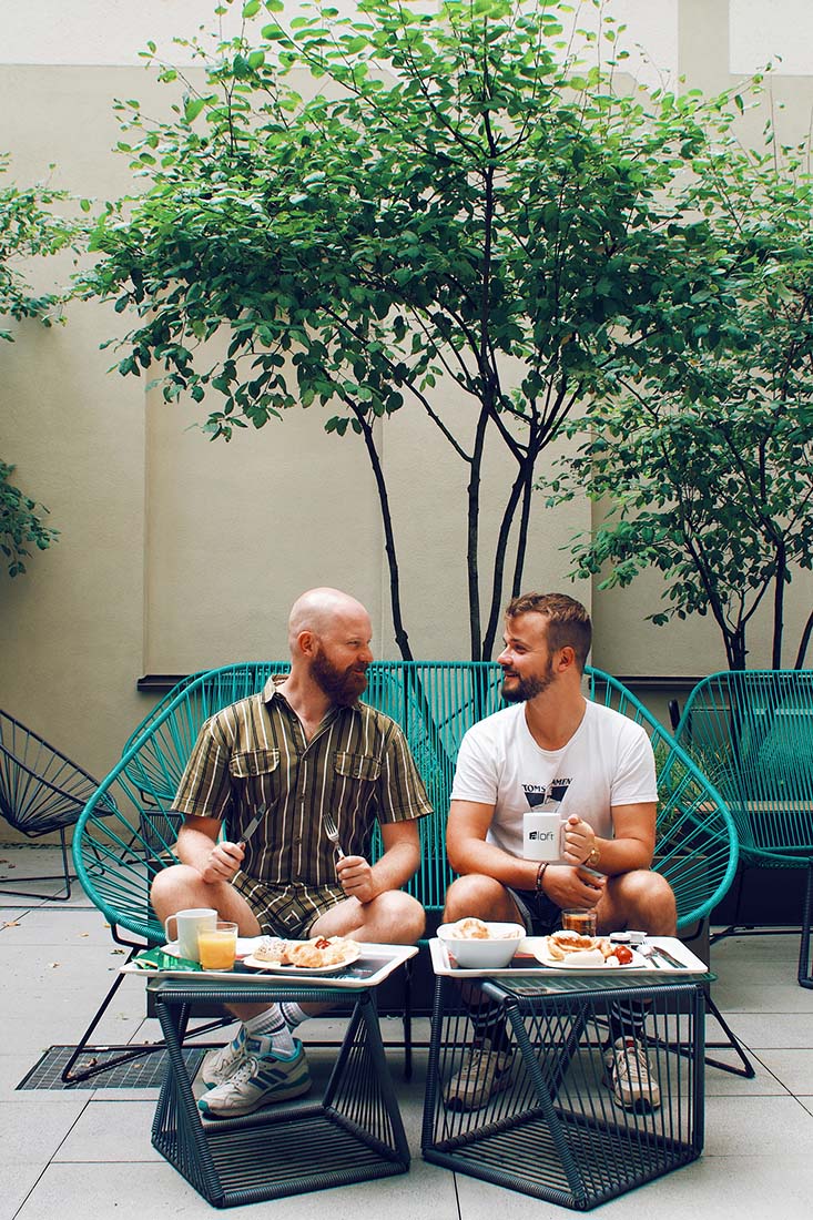 The gay couple enjoying breakfast outside in the inner courtyard of the LGBTQ+ friendly accommodation in Munich © Coupleofmen.com