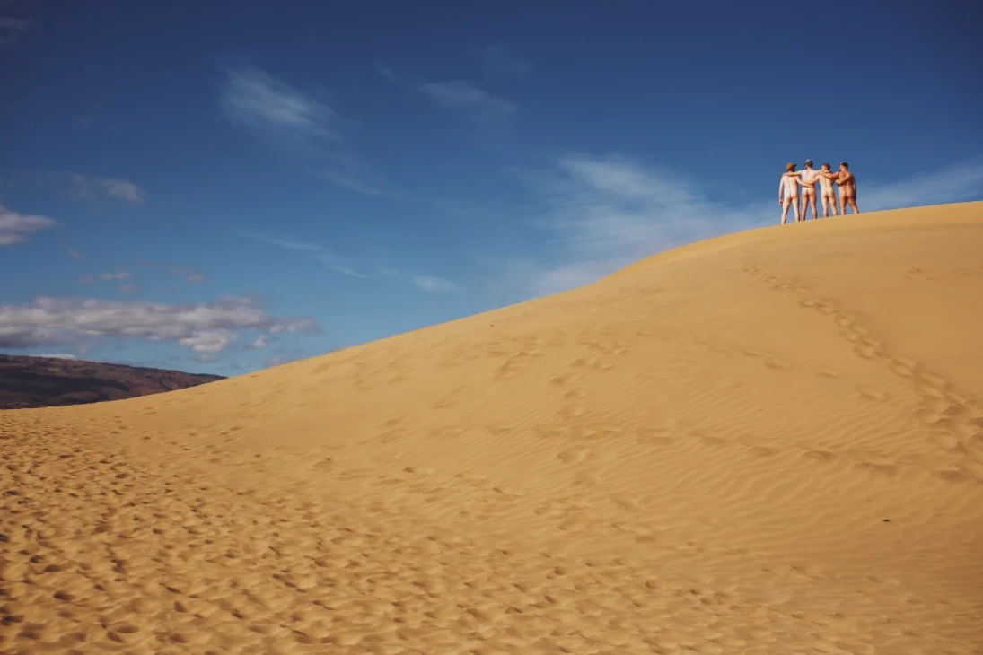 A couple of men standing on one of the Maspalomas sand dunes on Gran Canaria while wearing nothing but their hats.