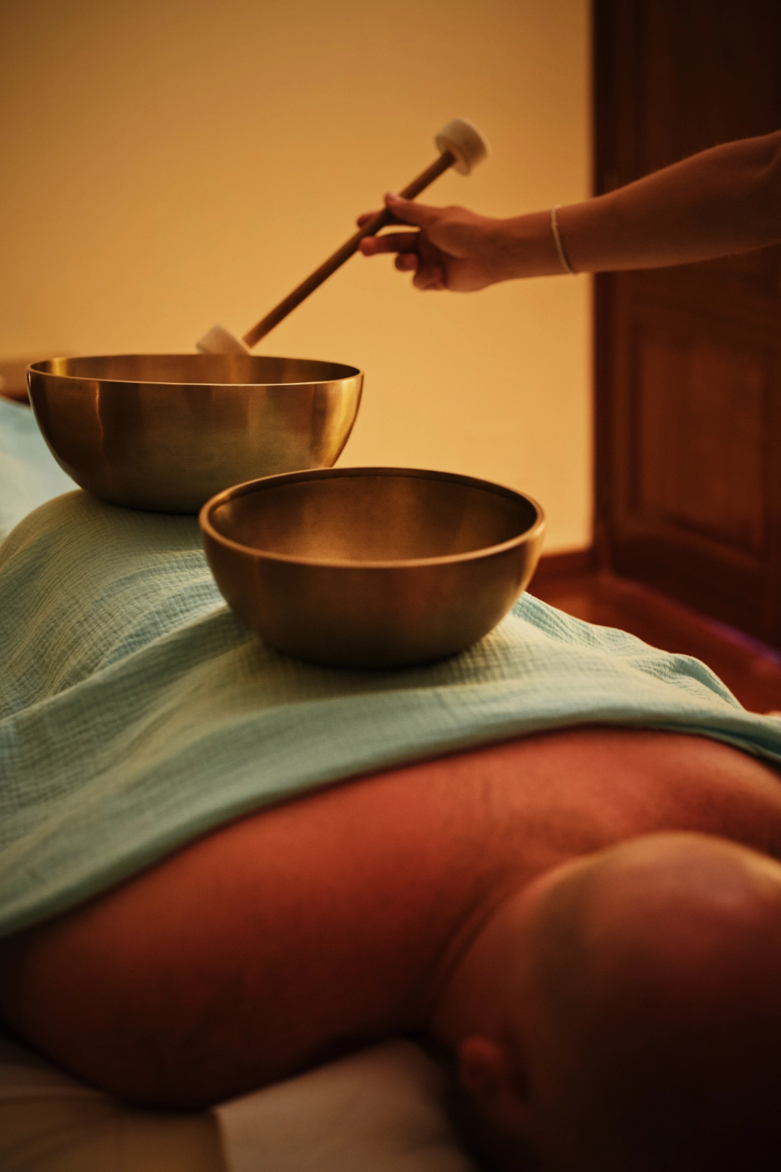 A men is laying naked under a blue blanket while enjoying a relaxing singing bowl massage.