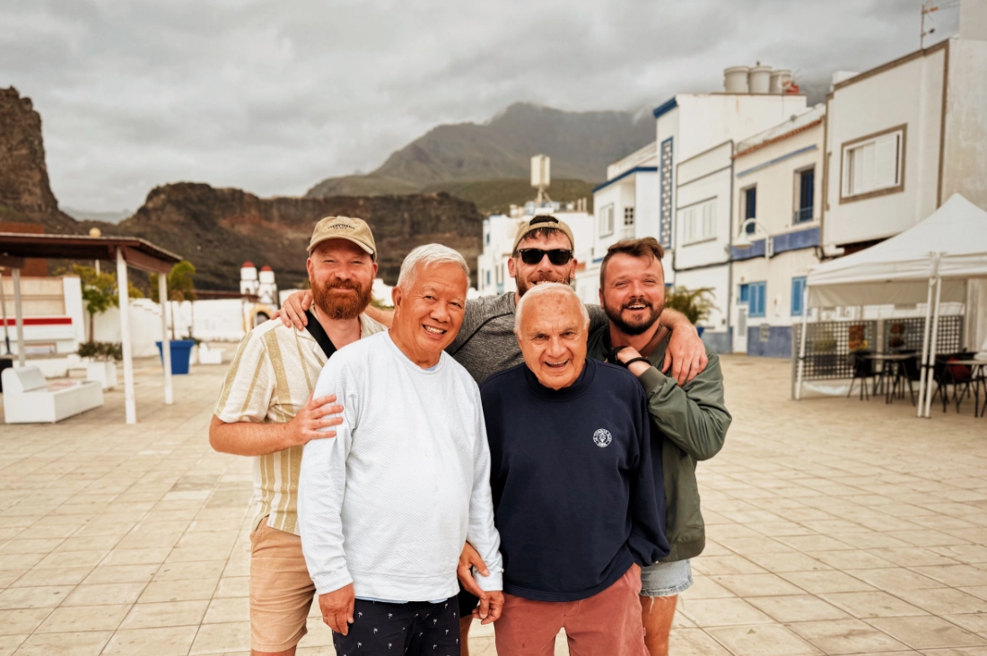 five men posing for the picture with a small fishers village and the mountains of Gran Canaria in the background,