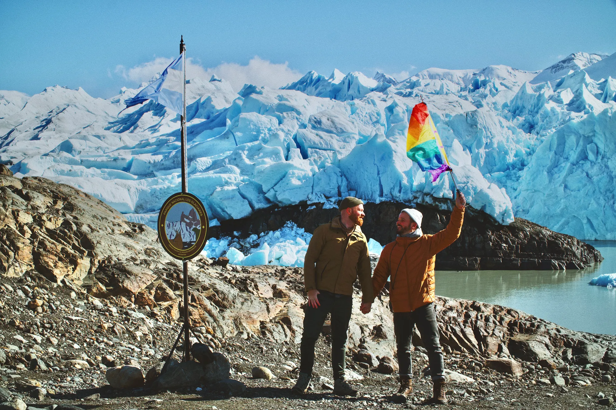 Waving the rainbow flag next to a Parque Nacional Los Glaciares board © Coupleofmen.com El Calafate gay travel