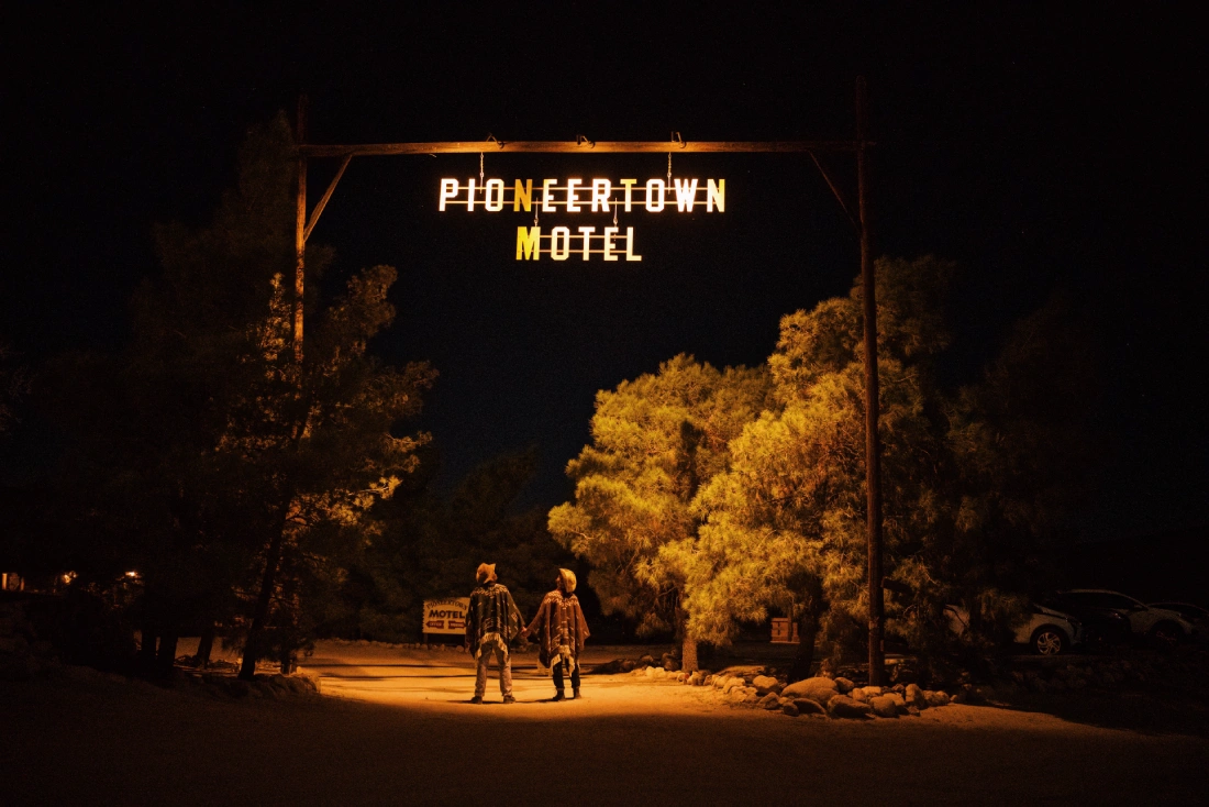 Two gay cowboys hand in hand under the Pioneertown Motel sign by night © Coupleofmen.com
