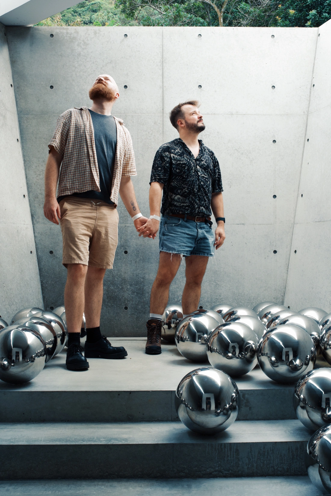 We are standing hand in hand surrounded by the reflective silver spheres across concrete stairs, an installation of Yayoi Kusama&rsquo;s Narcissus Garden in the Tadao Ando designed Valley Gallery
